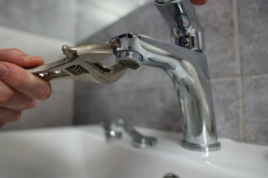 Photo of Plumber repairing metal faucet with spanner in bathroom, closeup