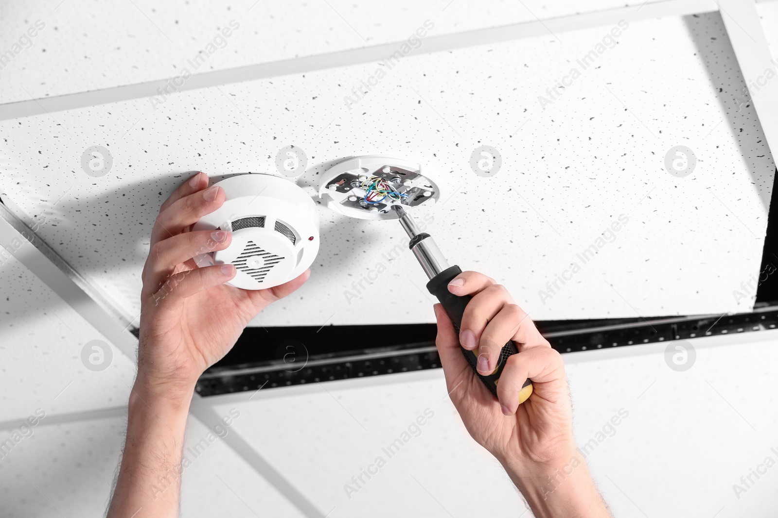 Photo of Young male technician installing smoke alarm system indoors