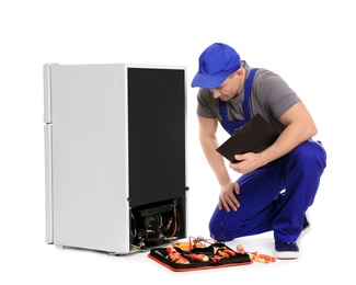 Male technician with clipboard and tools near broken refrigerator on white background