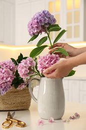 Woman making bouquet with beautiful hydrangea flowers at table indoors, closeup. Interior design element