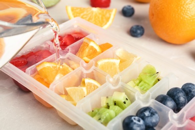 Photo of Pouring water into ice cube tray with different fruits and berries on table, closeup