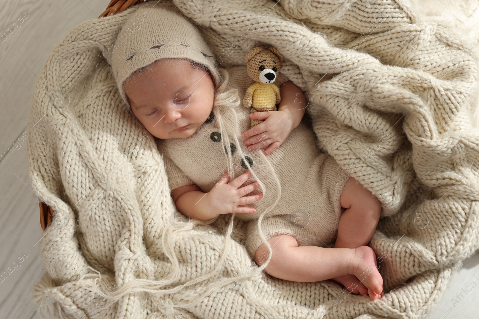 Photo of Adorable newborn baby with toy bear sleeping in wicker basket, top view