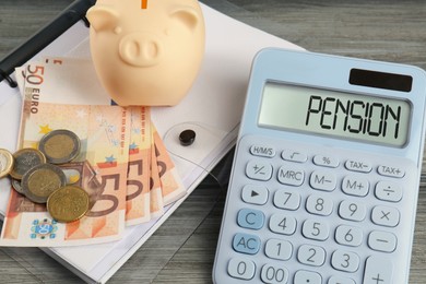 Photo of Calculator, piggy bank, euro banknotes, coins and folder on wooden table. Pension planning