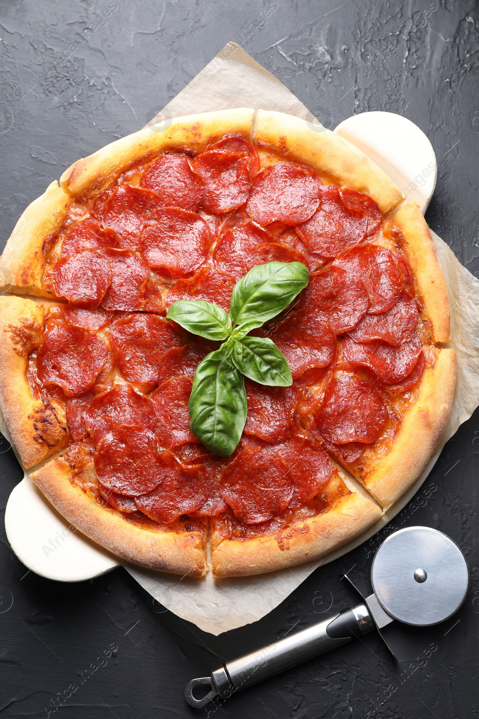 Photo of Tasty pepperoni pizza and cutter on black textured table, flat lay