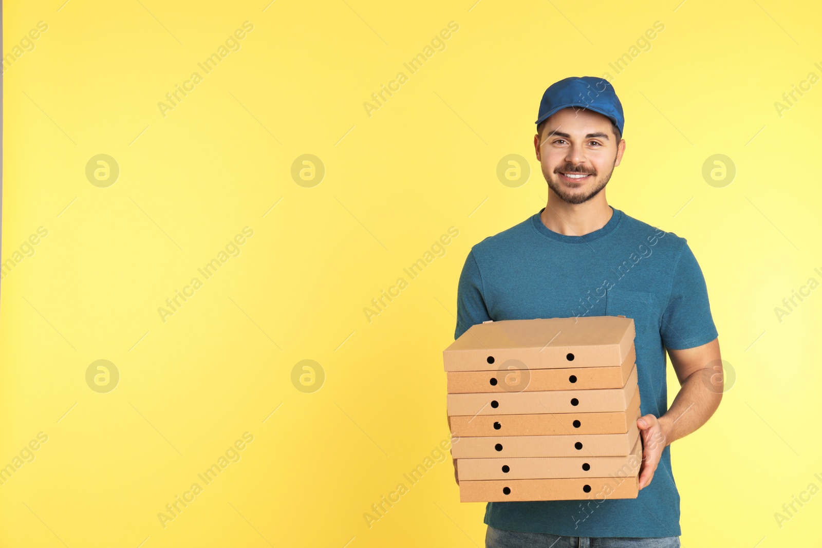 Photo of Young courier with pizza boxes on color background, space for text. Food delivery service