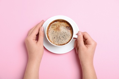 Woman with cup of coffee on pink background, top view