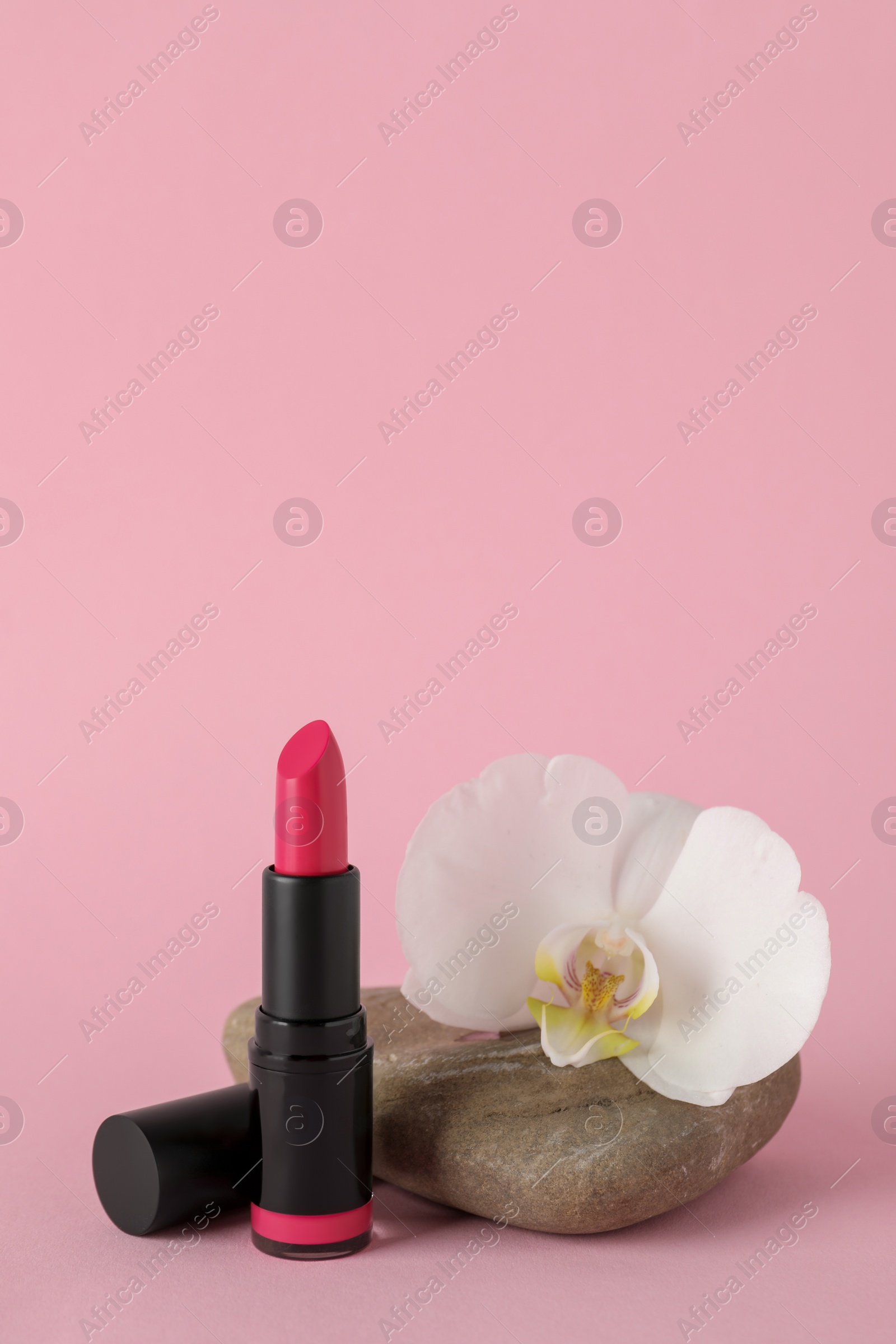 Photo of Beautiful lipstick and orchid flower on stone against pink background