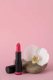 Beautiful lipstick and orchid flower on stone against pink background
