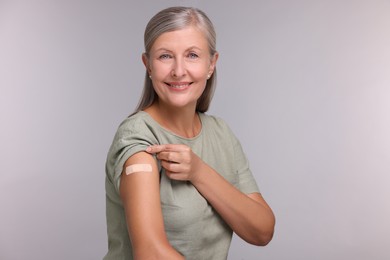 Photo of Senior woman with adhesive bandage on her arm after vaccination against light grey background