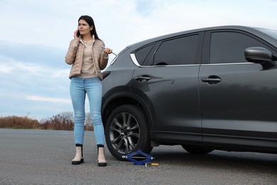 Photo of Worried young woman calling car service. Tire puncture
