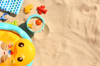 Photo of Flat lay composition with plastic beach toys and inflatable duck on sand. Space for text