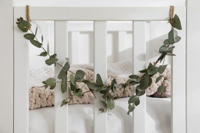 Comfortable crib decorated with beautiful eucalyptus garland in room