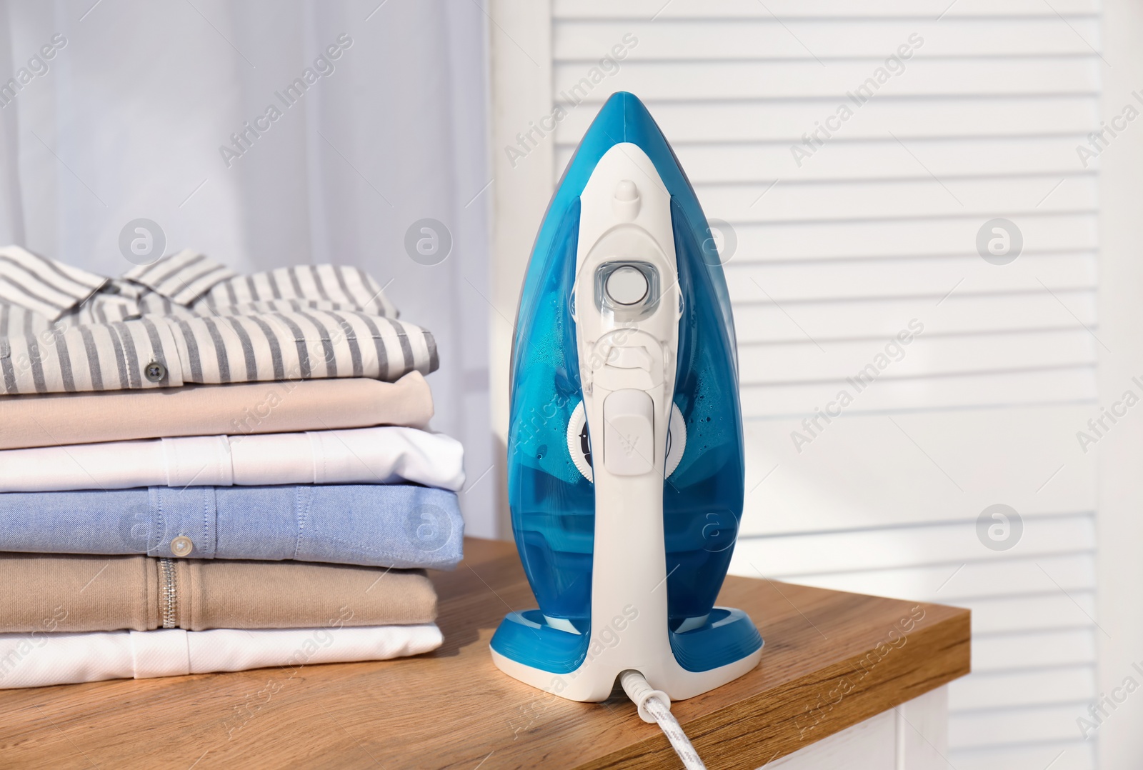 Photo of Stack of clean clothes and iron on board indoors