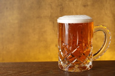 Photo of Mug with fresh beer on wooden table against yellow background, closeup. Space for text