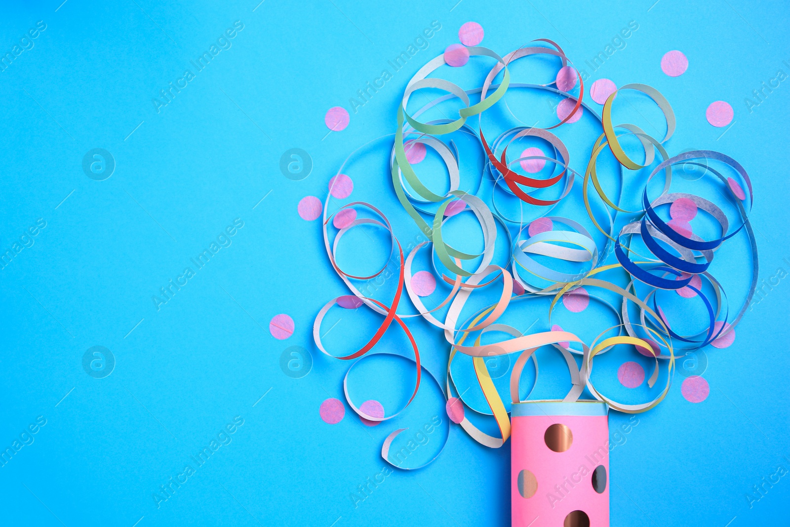 Photo of Beautiful serpentine and confetti bursting out of party popper on light blue background, flat lay. Space for text