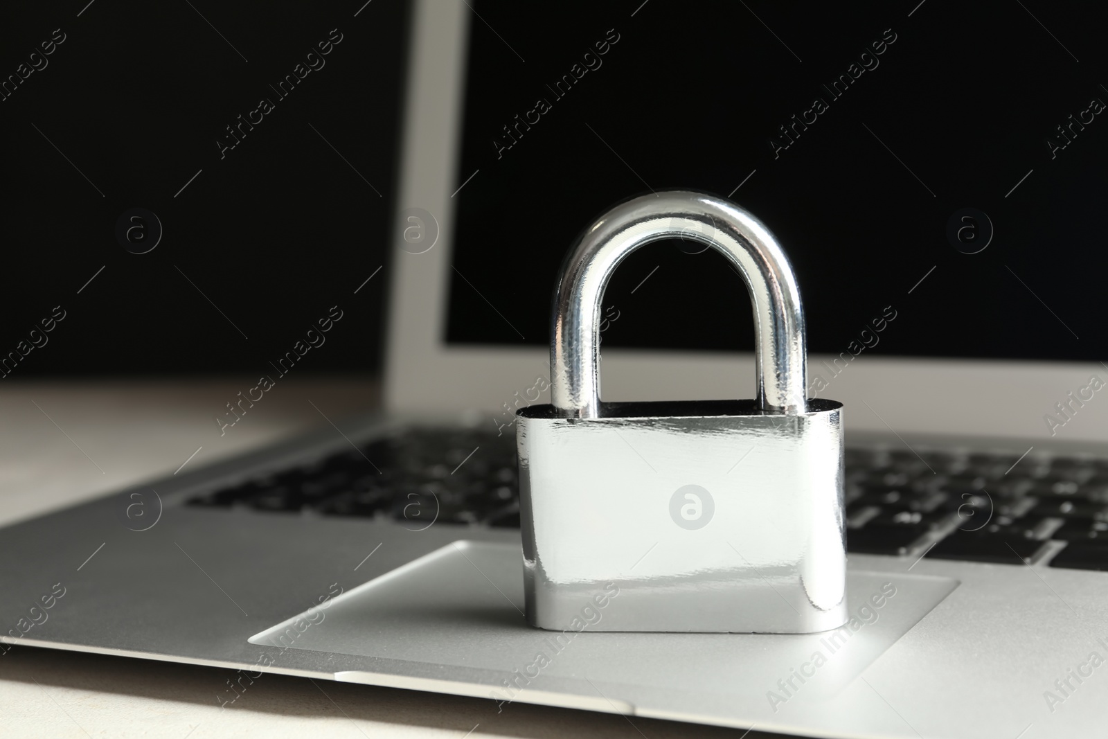 Photo of Metal lock and laptop on table, closeup. Protection from cyber attack