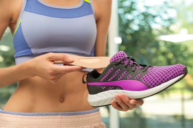 Woman putting orthopedic insole into shoe indoors, closeup. Foot care