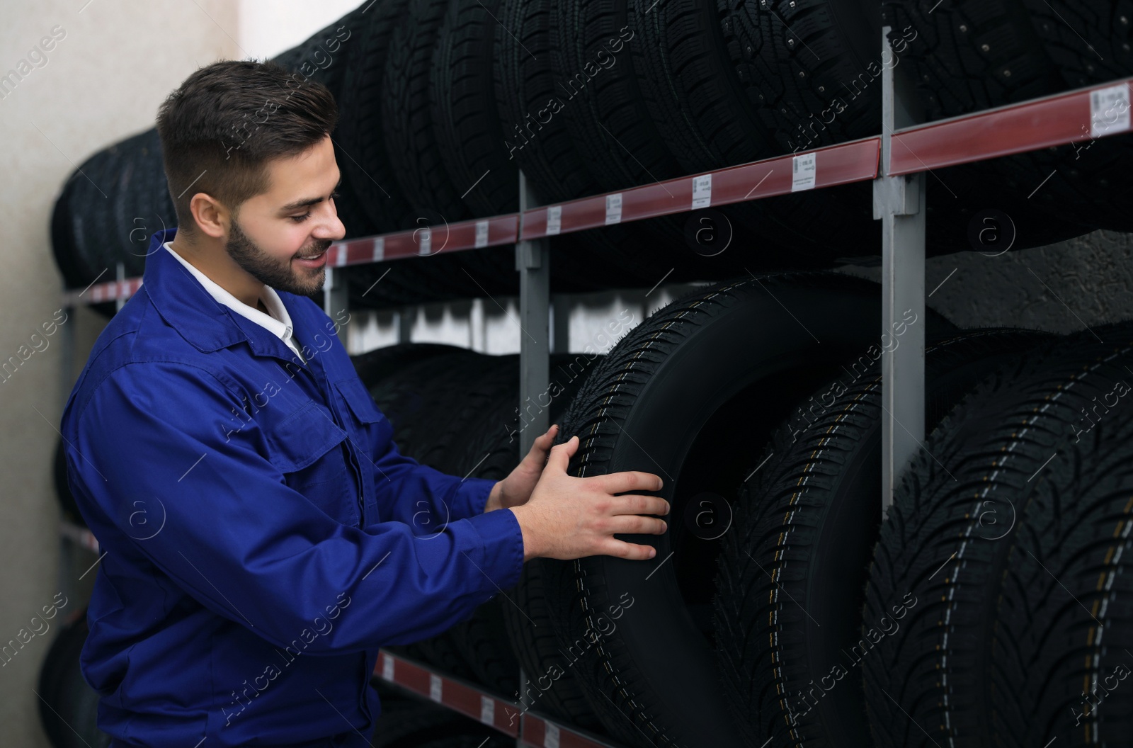 Photo of Male mechanic with car tire in auto store