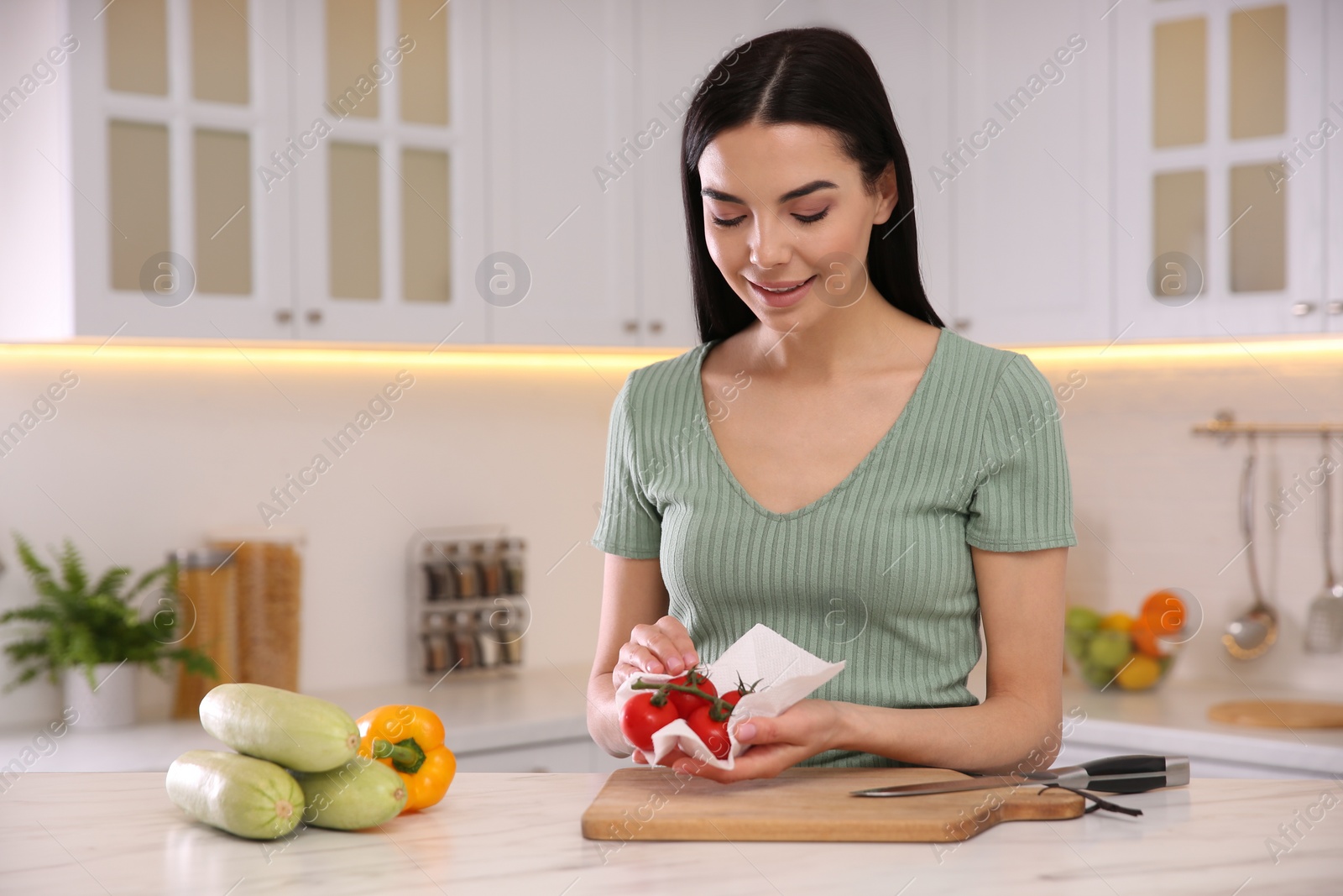 Photo of Woman wiping tomatoes with paper towel in kitchen