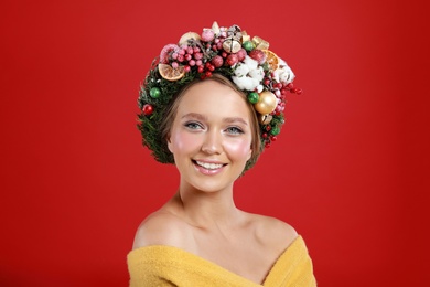 Beautiful young woman wearing Christmas wreath on red background