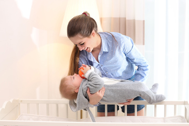 Photo of Teen nanny putting cute little baby in crib at home. Daytime sleep