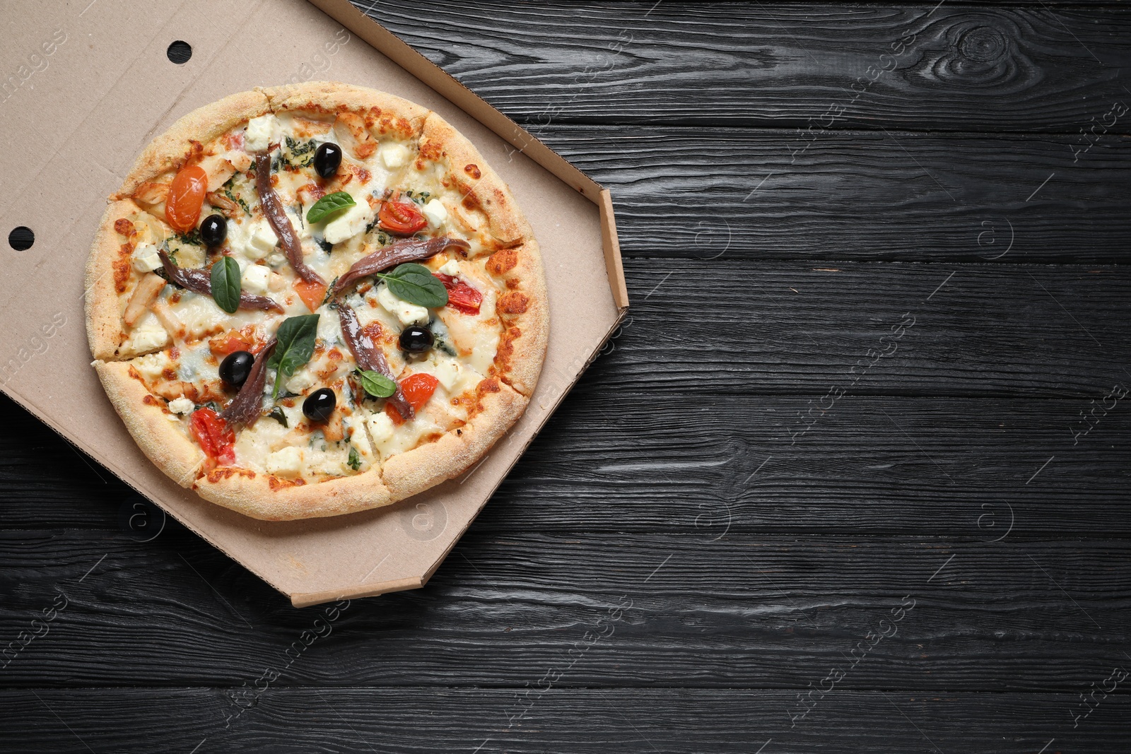 Photo of Tasty pizza with anchovies, basil and olives on black wooden table, top view. Space for text