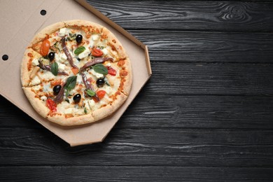 Photo of Tasty pizza with anchovies, basil and olives on black wooden table, top view. Space for text