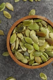 Photo of Wooden bowl with peeled pumpkin seeds on grey table, flat lay