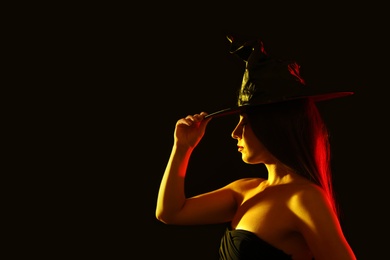 Photo of Young woman wearing witch costume on black background, space for text. Halloween party