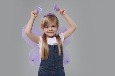 Photo of Cute little girl in fairy costume with violet wings on light grey background