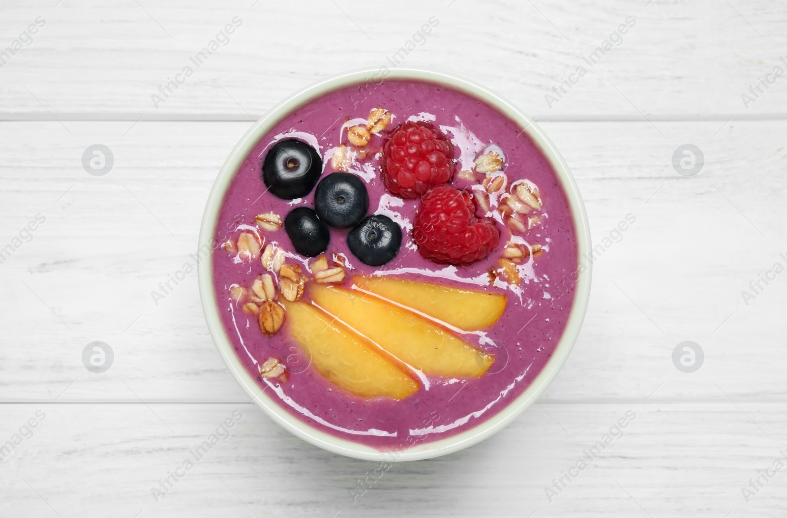 Photo of Delicious acai smoothie with peach slices and oatmeal on white wooden table, top view