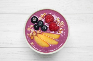 Photo of Delicious acai smoothie with peach slices and oatmeal on white wooden table, top view