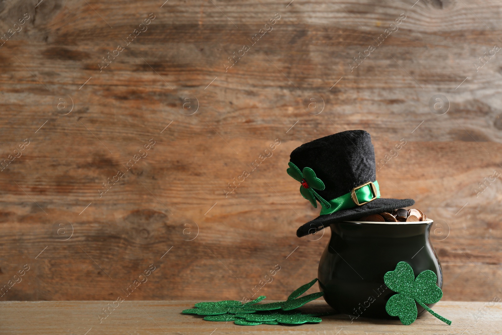 Photo of Pot of gold coins, hat and clover leaves on wooden table, space for text. St. Patrick's Day celebration