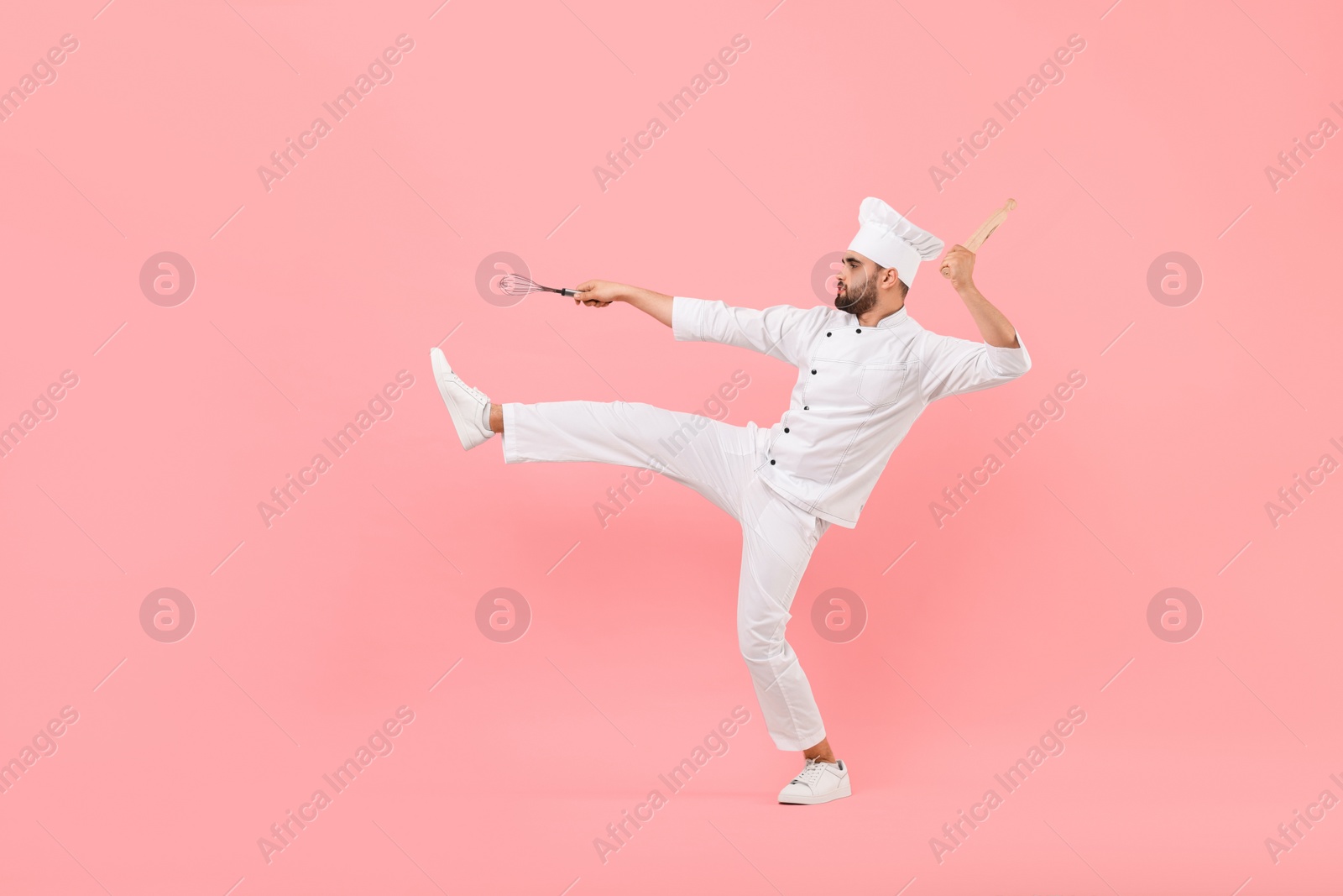 Photo of Professional chef holding kitchen utensils and having fun on pink background