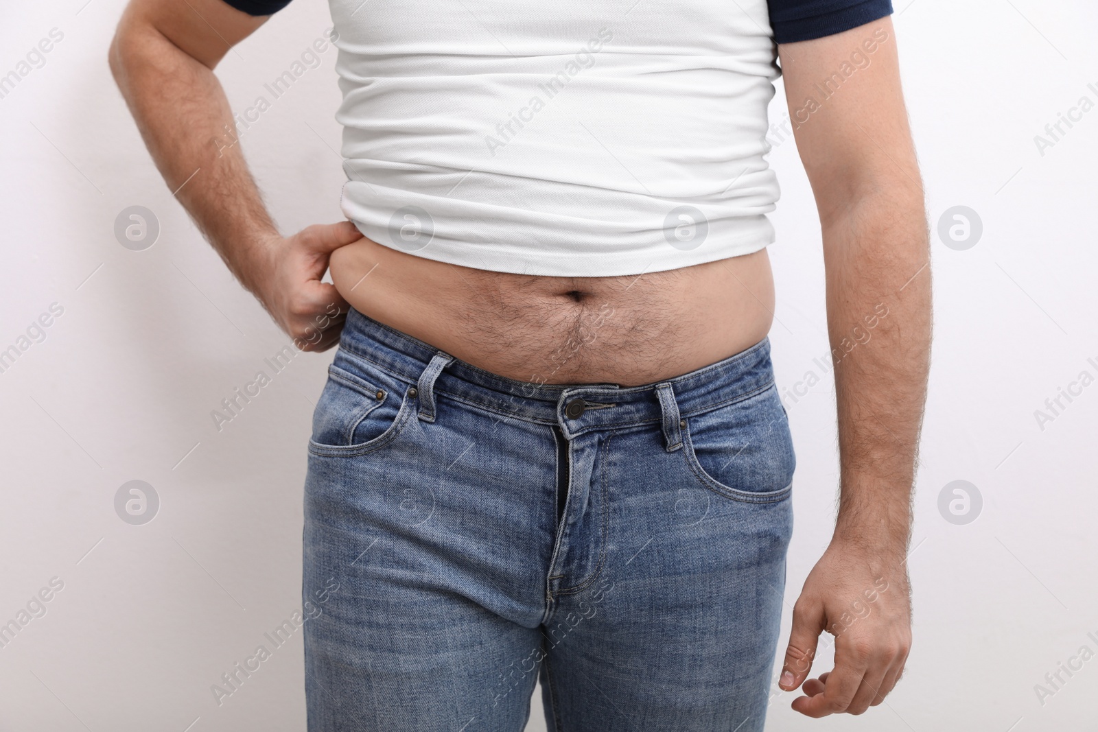 Photo of Man wearing tight t-shirt and jeans on white background, closeup. Overweight problem