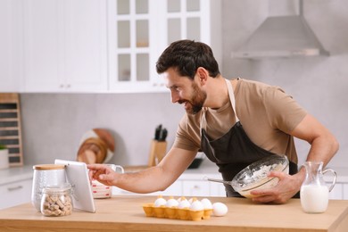 Man making dough while watching online cooking course via tablet in kitchen