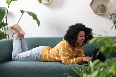 Photo of Relaxing atmosphere. Woman with laptop lying on sofa near houseplants in room