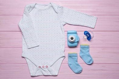 Baby clothes and camera on pink wooden background, flat lay