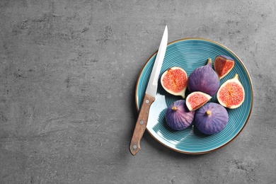 Photo of Plate with fresh ripe figs and knife on gray background, top view. Space for text