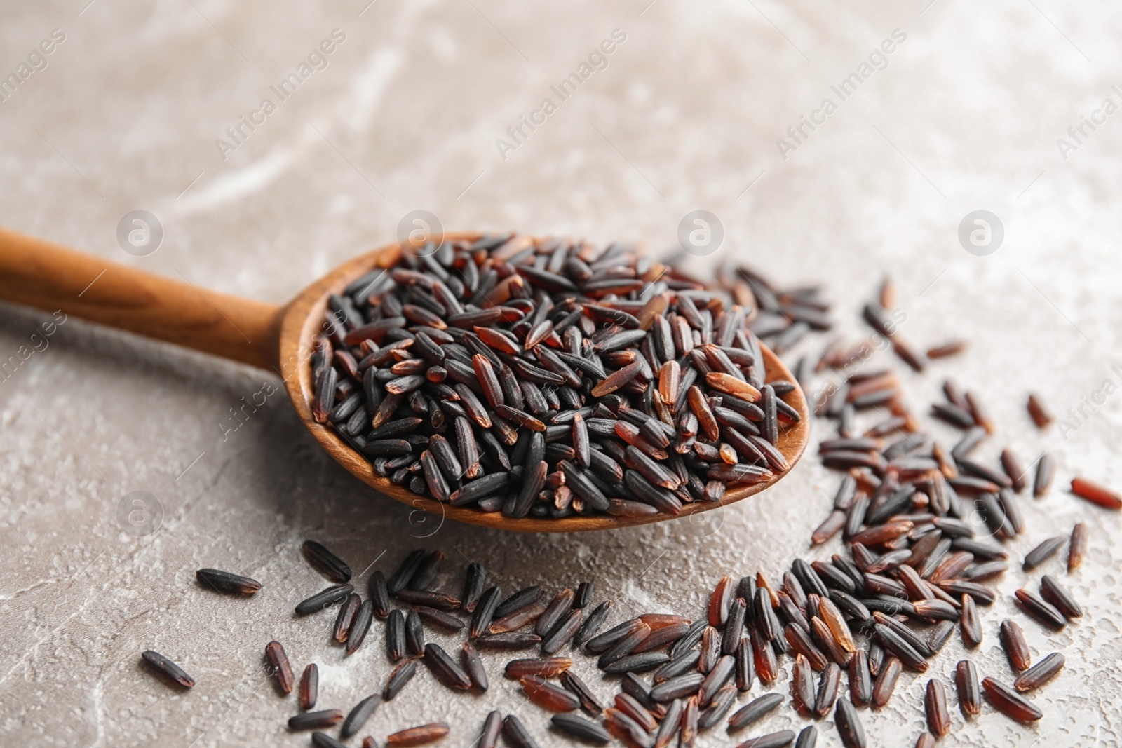 Photo of Spoon with uncooked black rice on grey background, closeup