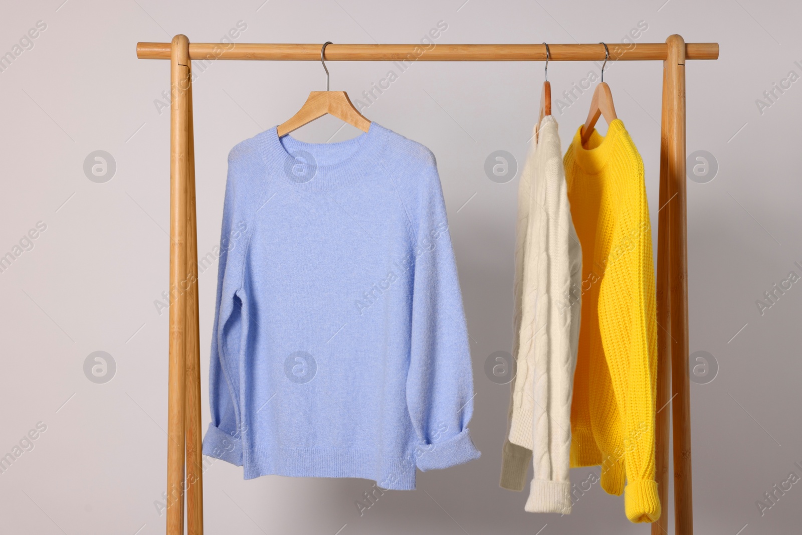 Photo of Rack with different warm sweaters on light background