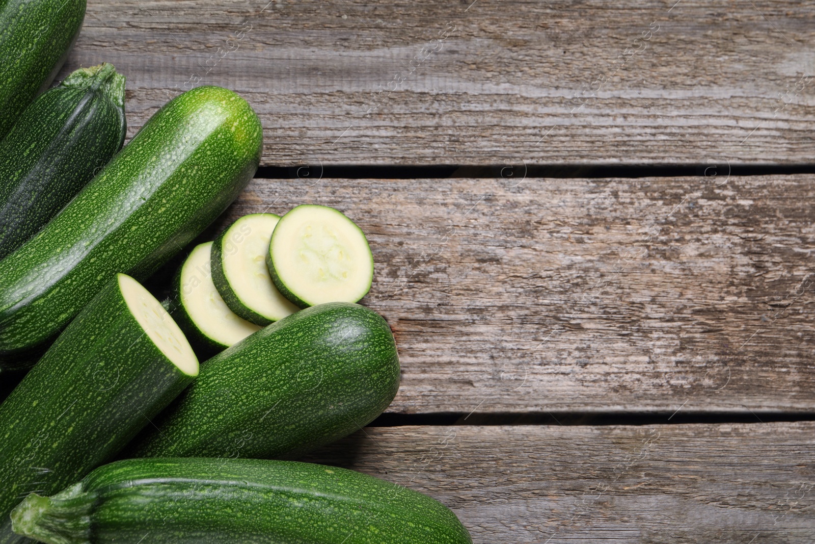 Photo of Whole and cut ripe zucchinis on wooden table, flat lay. Space for text