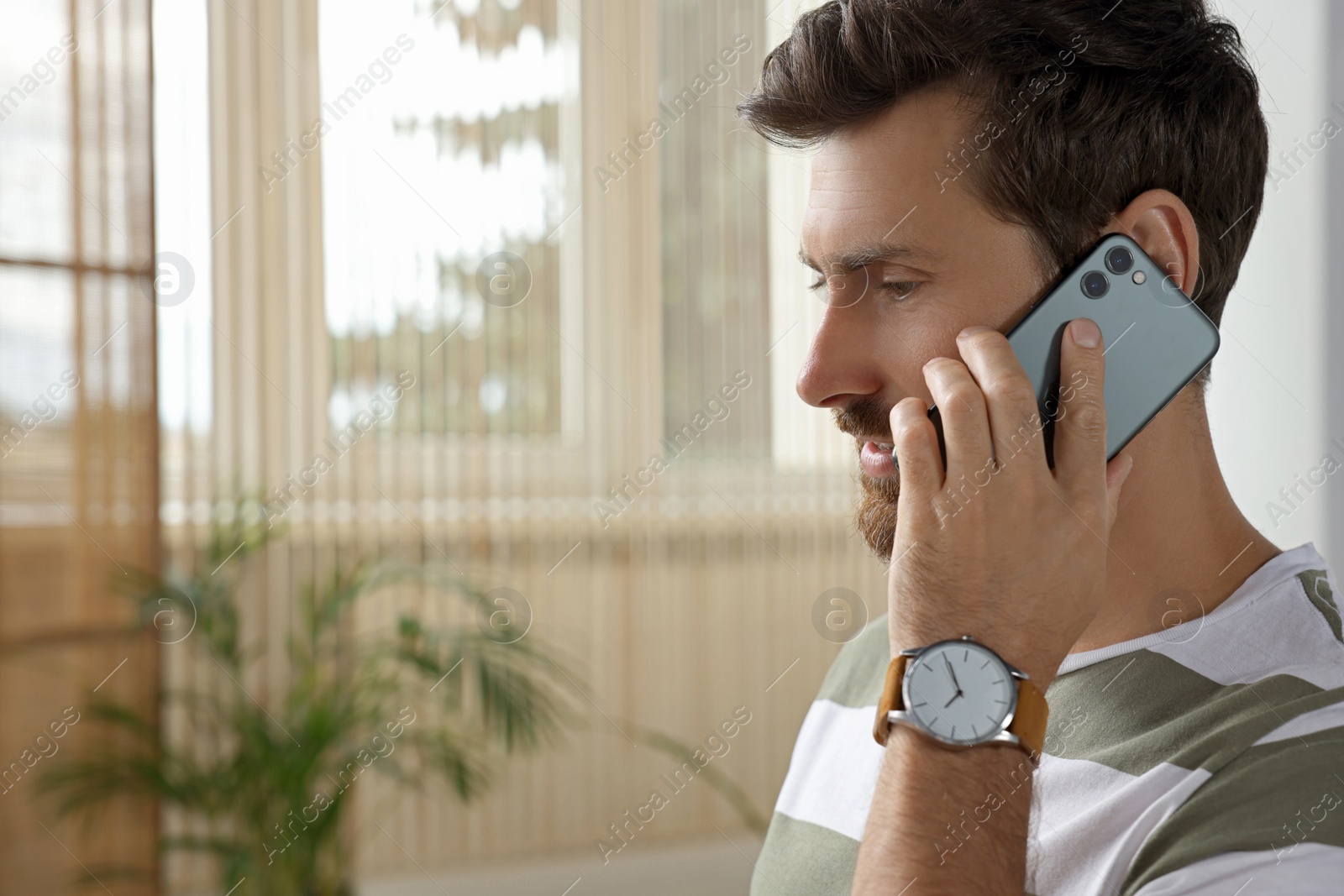 Photo of Handsome man talking on smartphone at home, space for text