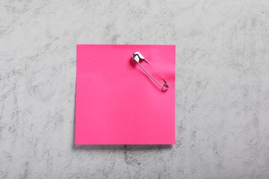 Photo of Pink paper note with safety pin on grey textured background, top view