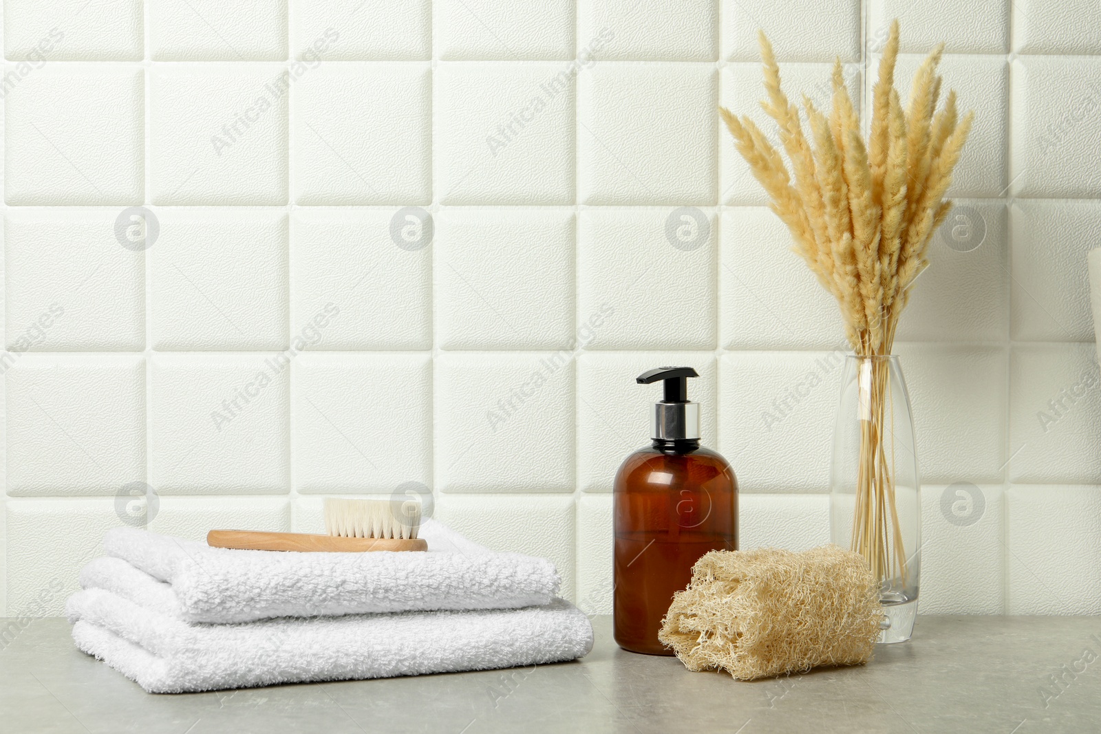 Photo of Different bath accessories, cosmetic bottle and spikelets in vase on gray table near white tiled wall