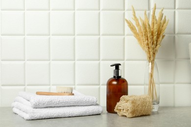 Photo of Different bath accessories, cosmetic bottle and spikelets in vase on gray table near white tiled wall