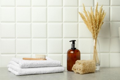 Different bath accessories, cosmetic bottle and spikelets in vase on gray table near white tiled wall