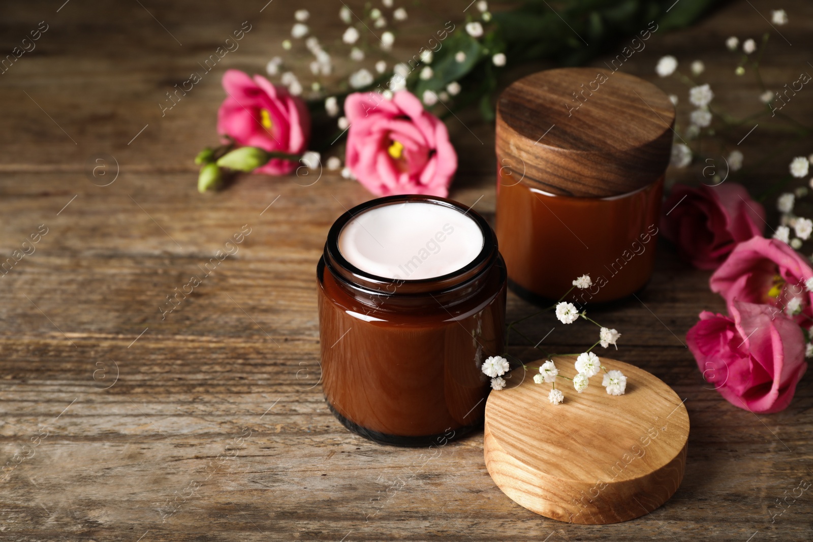 Photo of Jars of face cream and beautiful flowers on wooden table. Space for text