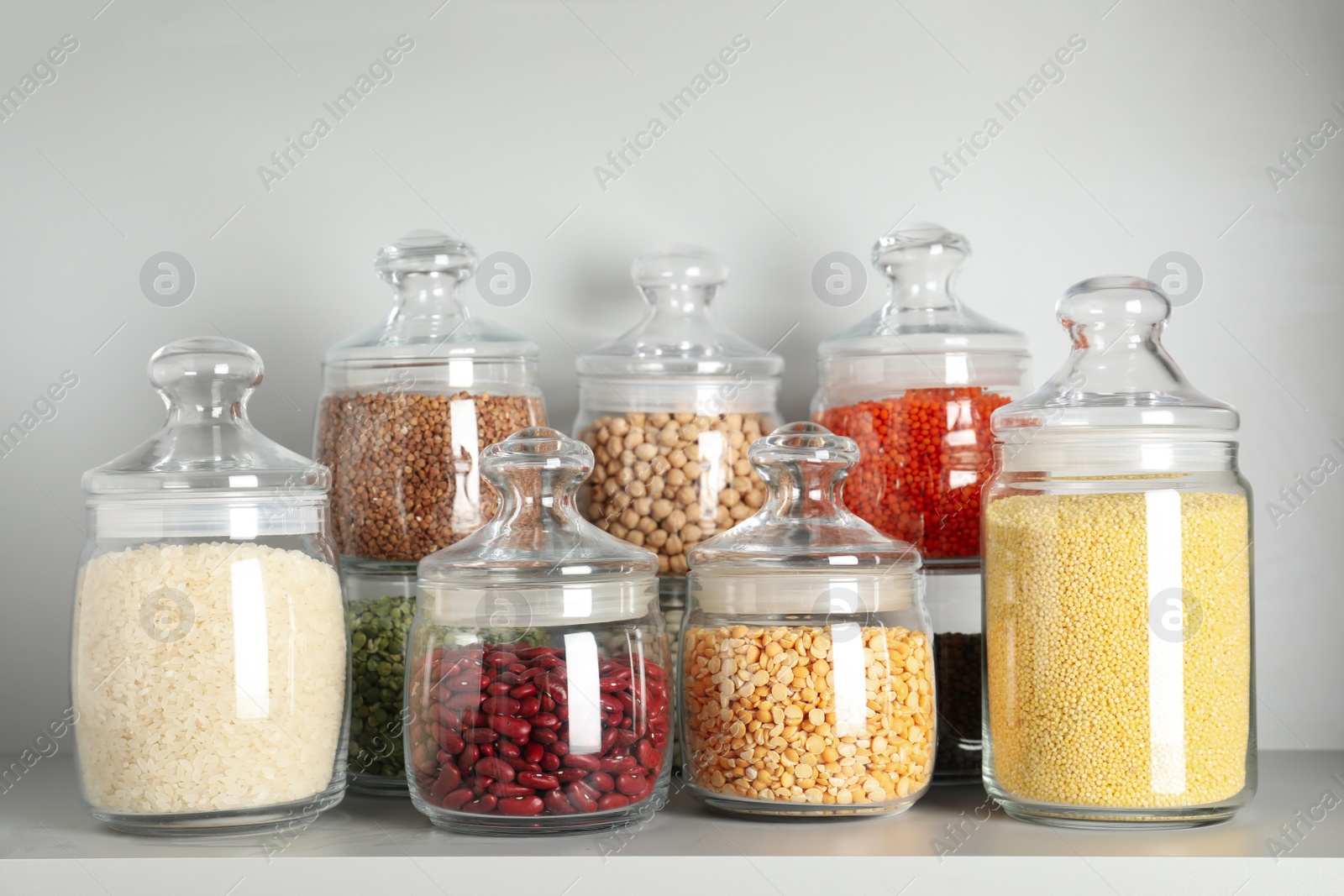 Photo of Glass jars with different types of groats and pasta on white shelf