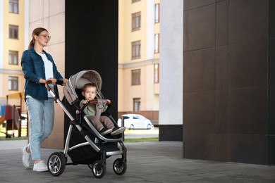 Photo of Beautiful nanny with cute little boy in stroller walking outdoors, space for text